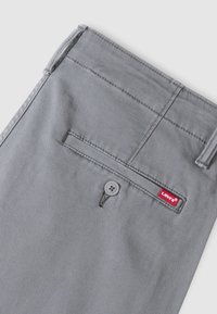 Poche de pantalon en tissu gris avec fermeture à bouton et étiquette rouge du logo Levi's cousue près du bord de la poche.