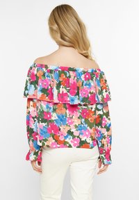 Blomsteret off-shoulder top med rynket halsudskæring, prydet med lyse pink, blå og orange blomster på en grøn baggrund, lange ærmer og elastiske manchetter.
