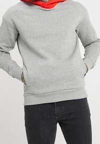 Grå sweatshirt med rund halsringning, långa ärmar och ribbade muddar. Har en avslappnad passform och en fleece-liknande textur. Bärs över mörka jeans.