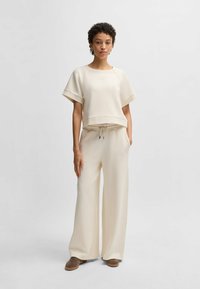 Light beige cropped sweatshirt with short sleeves and a drawstring waist, paired with wide-leg sweatpants in matching color. Soft texture.