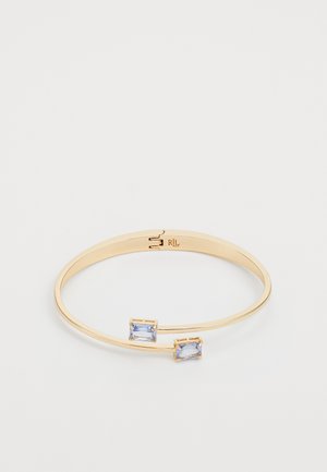 Kuldtooni metallist käevõru, millel on kaks ristküliku kujulist helesinist vääriskivi. Sile viimistlus ja siseruumis on graveeritud logo detail.