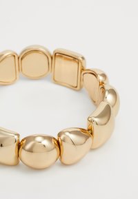 Bracciale color oro con maglie tonde e geometriche, finitura metallica lucida. Texture liscia e forme diverse, tra cui quadrati e ovali.