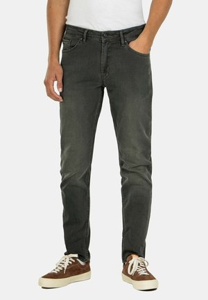 Dunkelgraue Denim-Jeans mit schmaler Passform, fünf Taschen und sichtbaren Nähdetails. Getragen mit braunen Wildledersneakers und einem weißen Hemd.