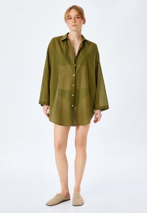 Olijfgroene linnen shirt, met knopen, lange mouwen, voorzakken, gebogen zoom. Draagt met beige instappers.