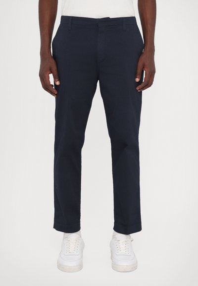 Navyblauwe katoenen chino-broeken met een gestroomlijnd ontwerp, voorzien van een vlakke voorkant, riemlussen en taps toelopende benen, gecombineerd met witte sneakers.