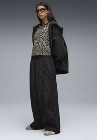 Svart oversized hoodie över en leopardmönstrad långärmad topp, parat med lösa svarta byxor och beigea slideskor med logotypdetaljer.