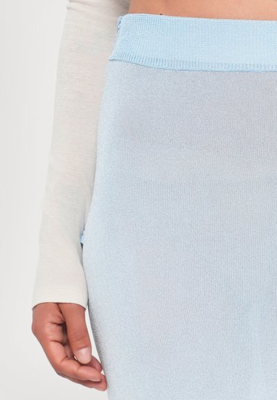 Saia de malha canelada azul-claro com uma cintura larga; textura suave e design ajustado ao corpo. Mão posicionada sobre a saia.