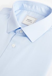 Svetlomodrá pánska košeľa vyrobená z hladkej tkaniny, so špicatým golierom, zapínaním na biele gombíky a štítkom "NEXT Tailoring".