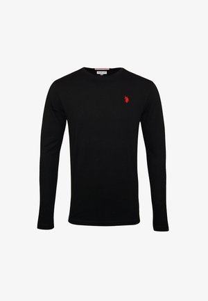 Chemise noire à manches longues avec un petit logo rouge sur la poitrine, associée à un jean bleu et des baskets noires avec des lacets blancs.