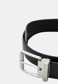 Cintura in pelle nera con superficie strutturata e fibbia in metallo argentato con design rettangolare e meccanismo di chiusura scorrevole.