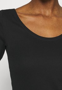 Svart långärmad topp med rundad halsringning, tillverkad av ett mjukt, flexibelt material med en slät yta, framhävt av en tajt passform.