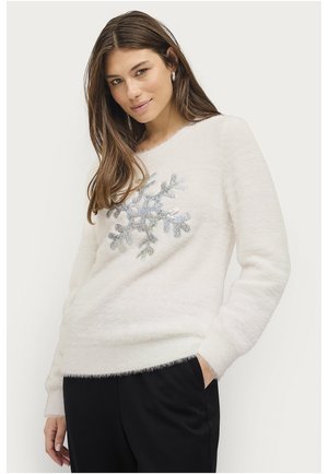 Witte, fluffy trui met een centraal, sprankelend sneeuwvlokontwerp. Zachte textuur met lange mouwen en een relaxte pasvorm. Zwarte broek.