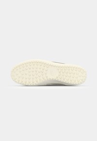 Sål af en sneakers, der har en struktureret hvid gummioverflade med små firkantede mønstre. Subtil branding er synlig.