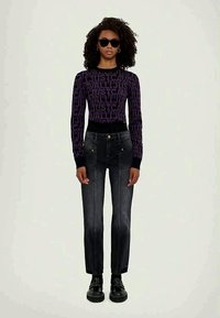 Jeans pretos com cintura ajustada, pernas retas e detalhes de costura clara. Combinados com uma blusa de manga longa com padrão roxo e óculos de sol.