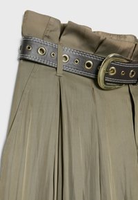 Jupe plissée kaki taille haute avec large ceinture marron foncé ornée d'une grande boucle dorée et d'œillets.