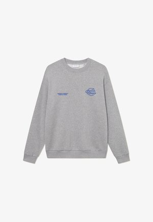 Sivi dukserica s okruglim izrezom, rebrastim manžetama i donjim rubom. Karakteriziraju je plavi vezeni logotipi na prsima i lijevom rukavu.