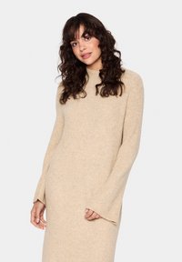 Abito in maglia beige con collo alto e ampie maniche a campana. Tessuto morbido con un motivo sottile su tutta la superficie. Fessure laterali per facilitare il movimento.
