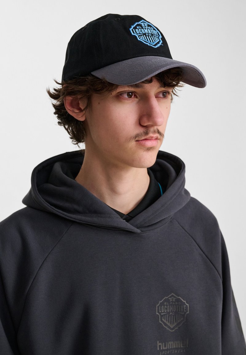 Svart baseballkeps med grå skärm, med en blå och svart broderad logotyp. Grå sweatshirt med en diskret logotyp på bröstet.