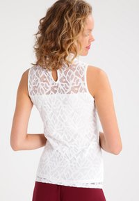 White sleeveless top featuring a floral lace design, a keyhole back, and a soft texture. Bottom has a simple, straight cut.