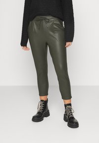 Pantalons en simili cuir vert olive avec une taille à cordon, présentant des jambes fuselées et des coutures latérales, associés à des bottines noires à lacets.