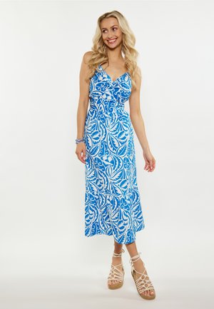 Rochie maxi cu imprimeu floral în nuanțe de albastru și alb, cu decolteu în V, bretele reglabile și tiv în straturi. Modelul poartă sandale espadrile cu barete.