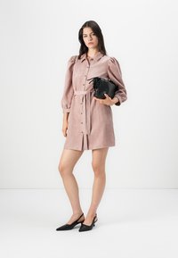 Rozā korduroja kleita ar uzpūstām piedurknēm, pogu priekšpusi un sasienamu jostu. Modelis tur melnu faktūru somu, apvienojot to ar melniem slingback zābakiem.