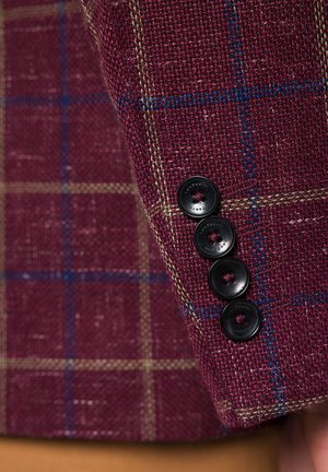 Bordowy materiał tweedowy w kratę z niebieskimi i beżowymi liniami, ozdobiony czterema czarnymi guzikami na mankiecie.