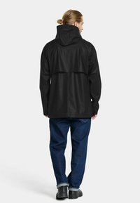 Svart vattentät jacka med huva, med en baksidesdesign. Matcher med blå denimjeans och svarta kängor.