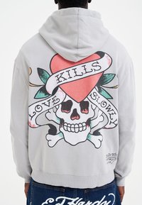 Grey hoodie featuring a large graphic of a skull, heart, and banner with text "LOVE KILLS SLOWLY" on the back. Soft material with a relaxed fit.