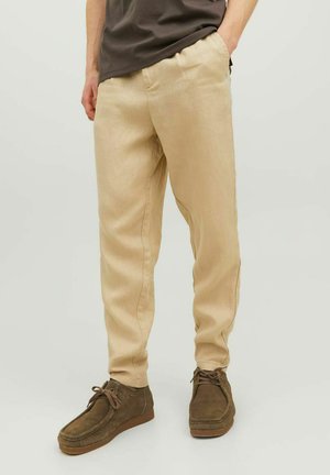Pantaloni di lino beige con una vestibilità affusolata, dotati di tasche laterali, orli cuffiati e abbinati a scarpe in suede marroni.