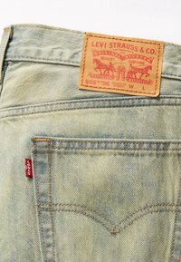 Světlemodré denimové džíny s hnědou koženou nášivkou s nápisem "Levi Strauss & Co." a červenou etiketou Levi's. Disponují švy a mají rovný střih.