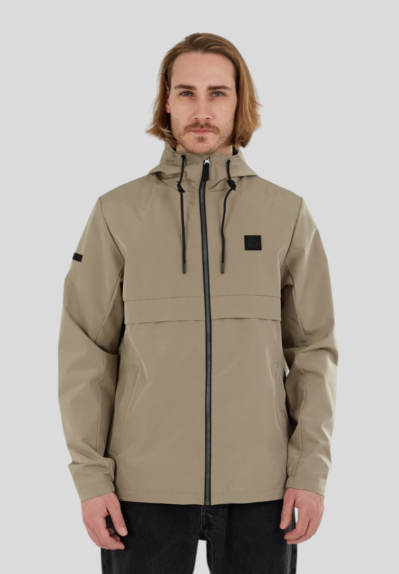 Beige wasserfeste Jacke mit Kapuze, Frontreißverschluss und schwarzen Akzenten. Verfügt über eine Brusttasche und zwei Seitentaschen, aus glattem, strapazierfähigem Material gefertigt.