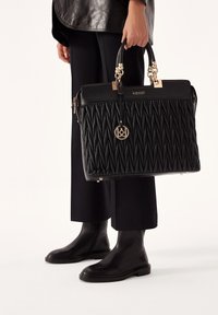 Czarna pikowana torebka skórzana z złotymi akcentami, górnymi uchwytami i dekoracyjnym breloczkiem. Noszona z czarnymi spodniami i botkami na kostkę.