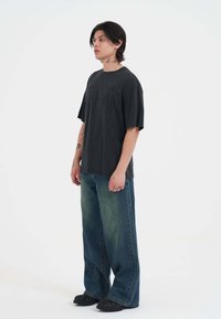 Czarna, oversize t-shirt z graficznym napisem, w połączeniu z dżinsami o szerokich nogawkach z wyblakłym zielonym gradientem. Czarnne buty dopełniają stylizację.