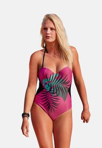 Maillot de bain une pièce avec un corps rose, des côtés noirs et un motif de feuille tropicale verte. Fabriqué en tissu extensible et lisse.