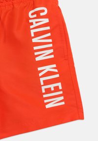 Φωτεινά πορτοκαλί σορτς Calvin Klein με κάθετο λευκό λογότυπο και πλαϊνή τσέπη στα δεξιά.