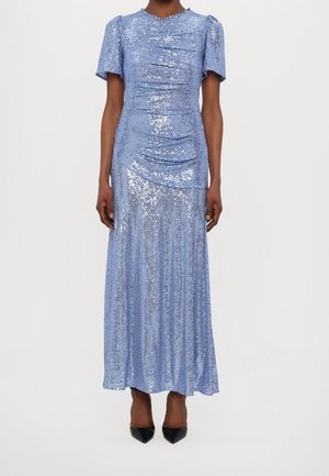 Hellblaues, kurzärmeliges Paillettenkleid mit gerafften Details, getragen mit schwarzen spitzen Pumps vor neutralem Hintergrund.