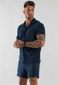 Marinblå, kortärmad skjorta med knapplist i strukturerad tyg med bröstficka; matchas med korta byxor, även de i marinblått.