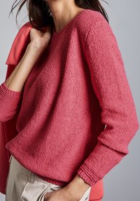 Rosa stickad tröja med en strukturerad yta, rund halsringning och långa ärmar. Matchad med beige byxor och en korallfärgad kavaj.