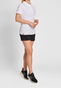 Vit kortärmad polo med knappslå, kombinerad med svarta sportshorts med en liten röd logotyp. Svarta sneakers med texturerad detalj.