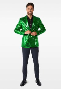 Blazer verde con paillettes e revers affilati, abbinato a pantaloni eleganti scuri e scarpe da cerimonia nere, caratterizzato da una vestibilità classica e un brillante luccichio.