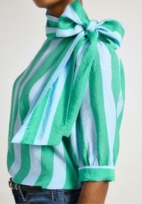 Grön och ljusblå randig blus med en stor rosett vid halsen, korta puffärmar och en texturerad kvalitet.