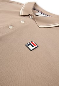 Beige polo shirt met witte gestreepte kraag, drie knopen en een klein geborduurd vierkant logo in marineblauw, rood en wit op de borst.