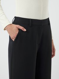 Félre szabott fekete nadrág sima tapintással, oldalzsebbel és lapos derékkal, övlyukakkal. Látható kontrasztvarrás.