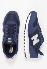 Marinblå träningsskor med meshupp, vadderad krage och vit gummisula. Har silverfärgad logotyp och svart halkskyddssula.