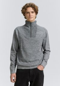 Pulover gri cu fermoar închis la jumătate, fabricat dintr-un material tricotat texturat, având guler înalt și manșete ribbate, asociat cu blugi negri.