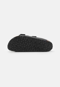 Black slip-on shoe with a textured rubber sole featuring a wave pattern, cork accents on the upper, and adjustable hook-and-loop straps.