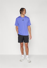 Purple short-sleeve athletic shirt with black logo, paired with black shorts and white athletic shoes. Simple design, lightweight fabric.