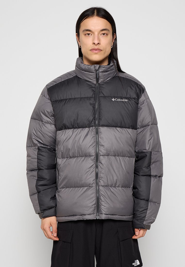 Chaqueta de plumón gris con un panel negro en el pecho, cuello alto, cierre de cremallera y costuras visibles. El material parece suave e insulated.