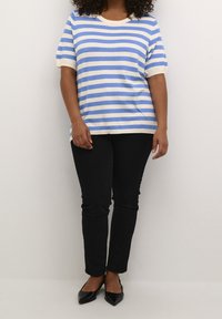 Gestreifter Kurzarm-Top in Blau und Creme, entspannter Schnitt, kombiniert mit schwarzen Slim-Fit-Hosen und spitzen schwarzen Ballerinas. Glatte, gestrickte Textur.